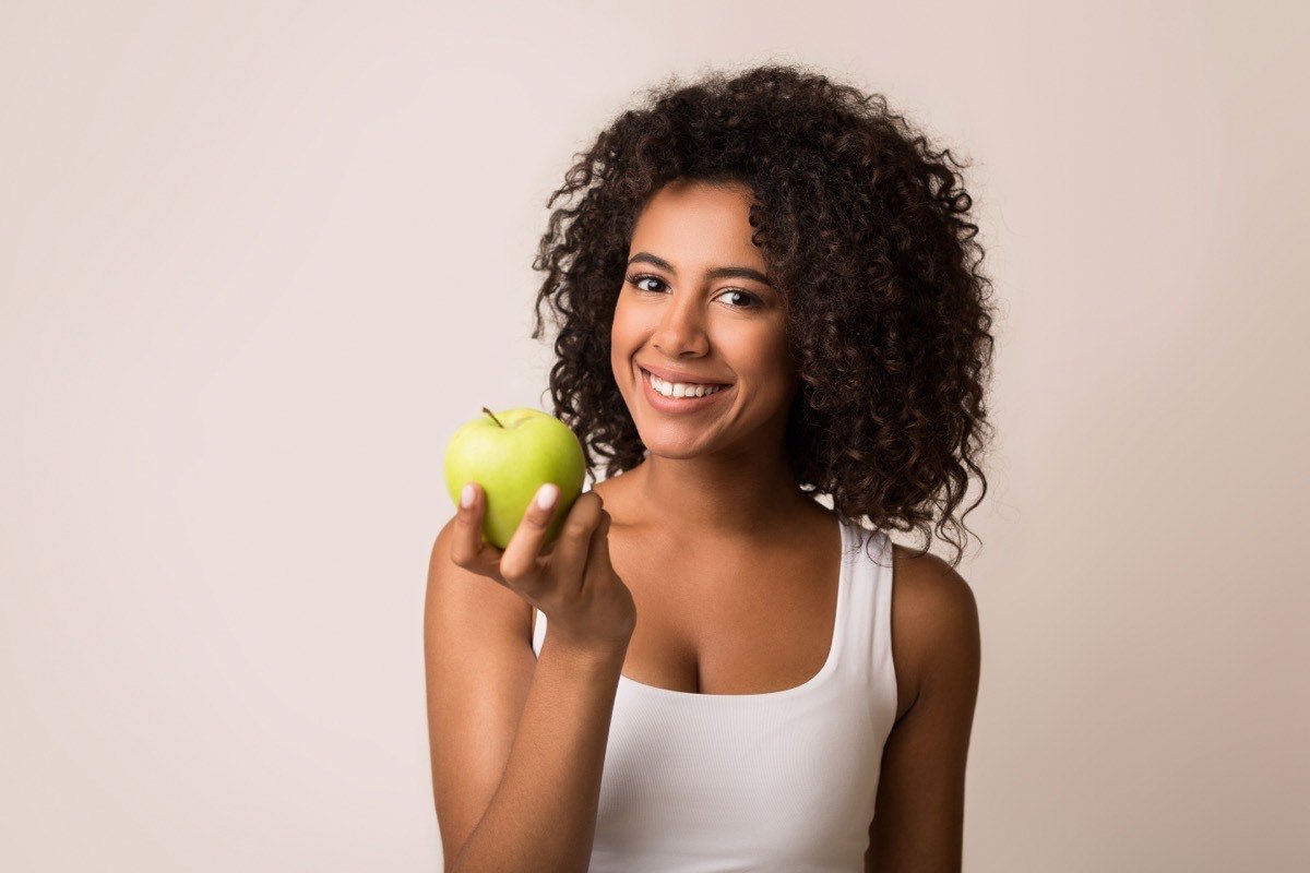 A smiling woman holding a fresh green apple