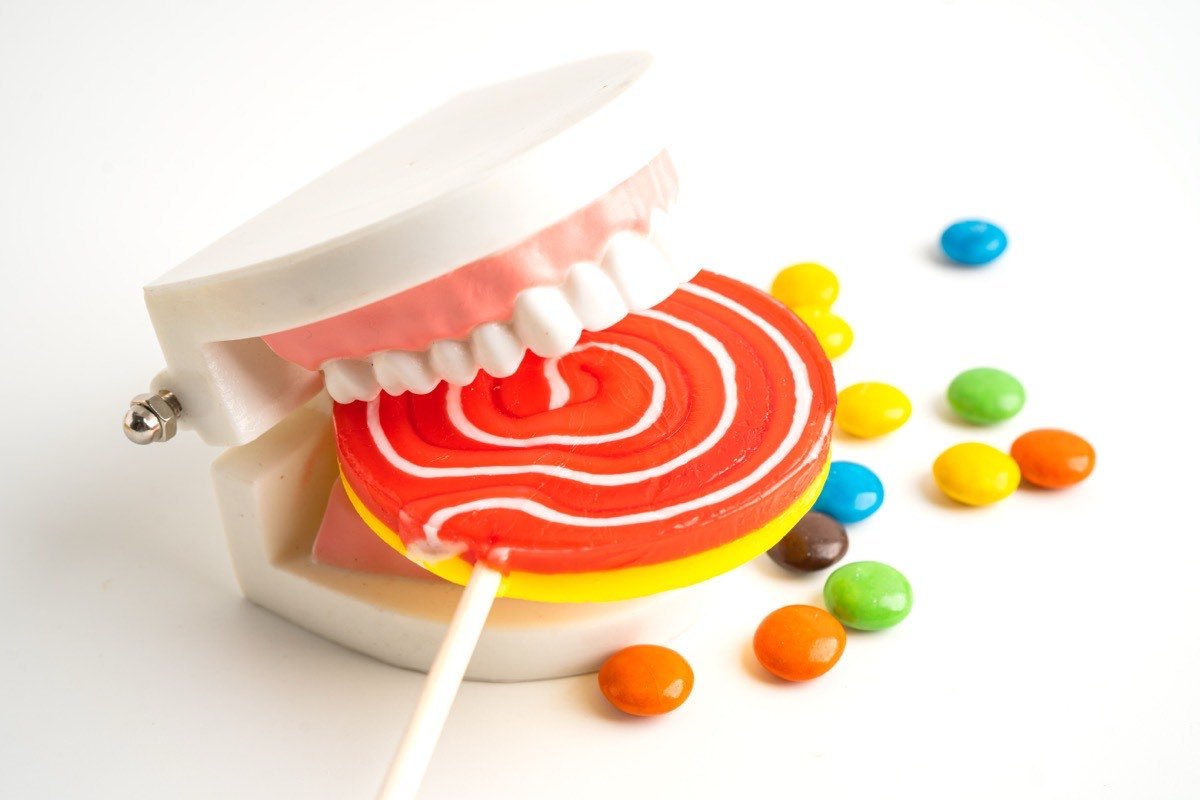 A dental model biting down on a lollipop, surrounded by scattered coloured sweets