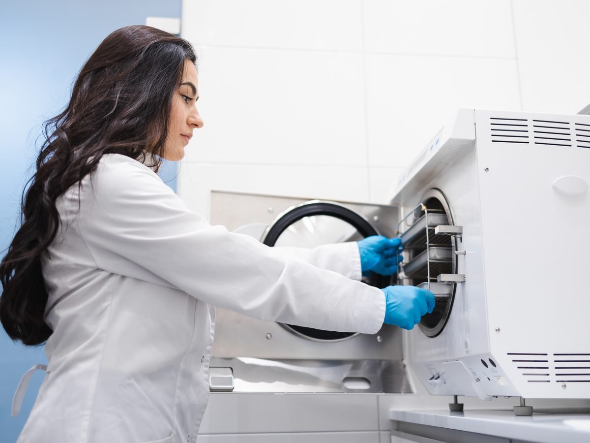 A dental sterilization technician loading instrument trays into an autoclave — part of our visible infection-control workflow