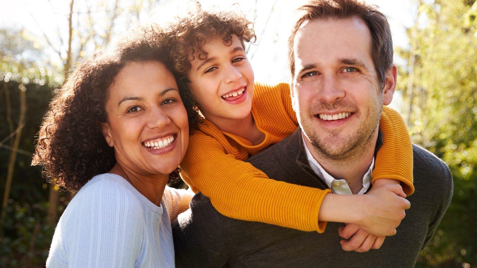A mother, father and young child laughing together outdoors